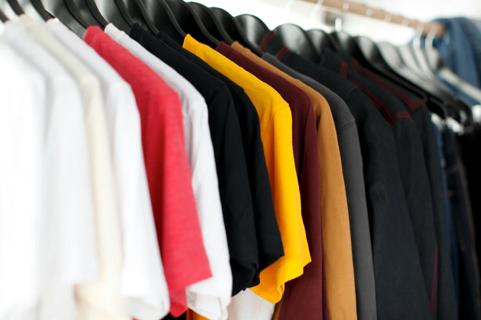 Kleiderstange mit unbedruckten Shirts in mehreren Farben — die Textilbasis vor der Veredelung